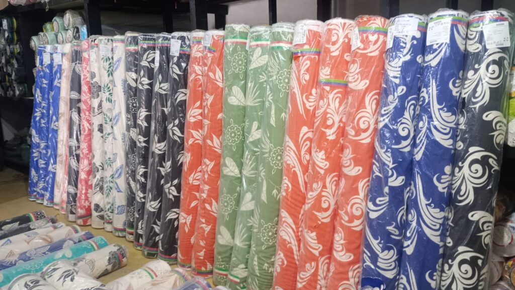 Diversas rolos de tecido com padrões florais em cores variadas, organizados verticalmente em estantes.