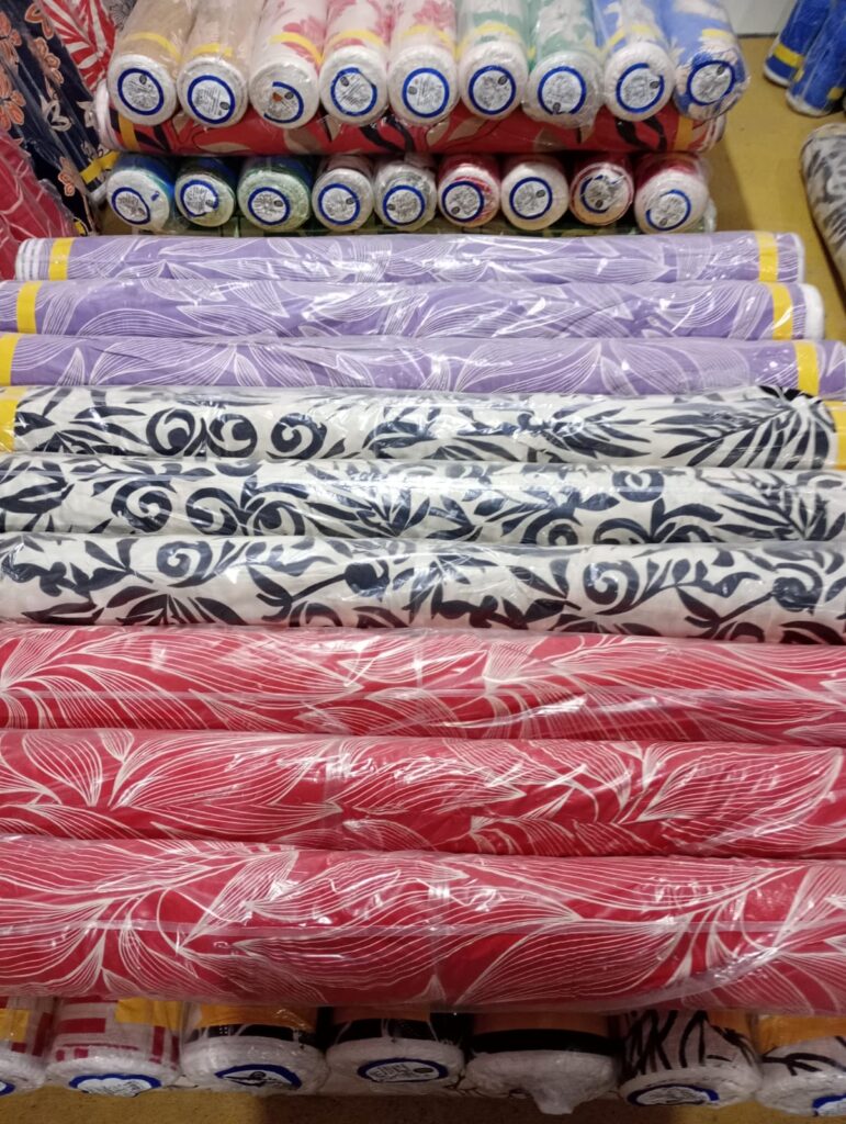 Rolos de tecido em várias cores e estampas, empilhados em uma loja de tecidos.
